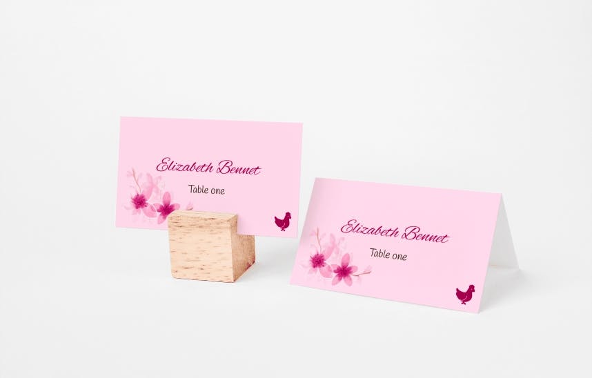 Rózsaszín esküvői ültetőkártya virágos és madaras mintákkal az asztali beállításokhoz, elegáns személyre szabottságot bemutatva.