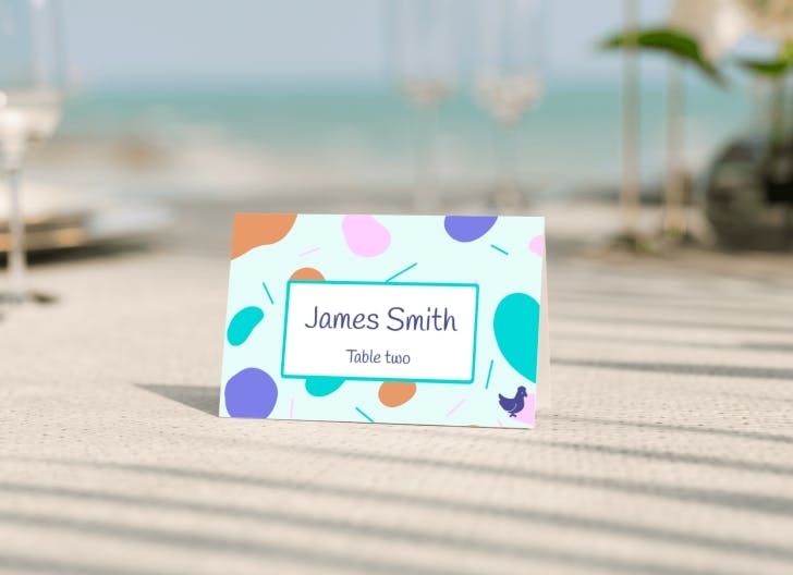 Colorful and modern place card with abstract design on a beach wedding table setup, ideal for vibrant wedding seating plans.